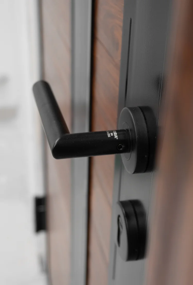 Detalle de manija o tirador negro de estilo moderno en una puerta de seguridad con acabado de madera.