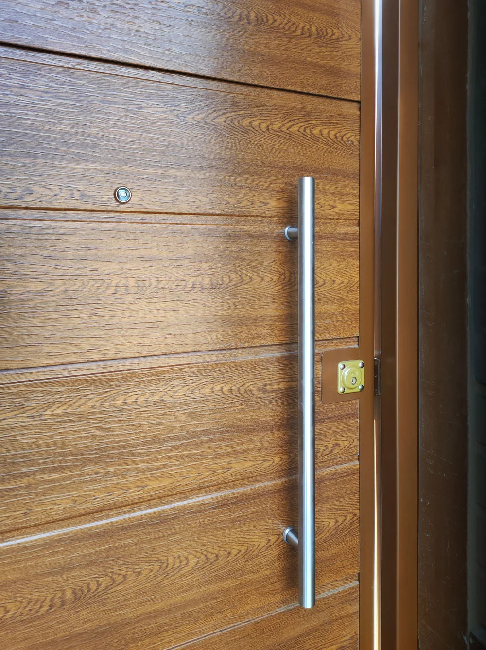 Primer plano de un manillón largo de acero sobre puerta de madera.